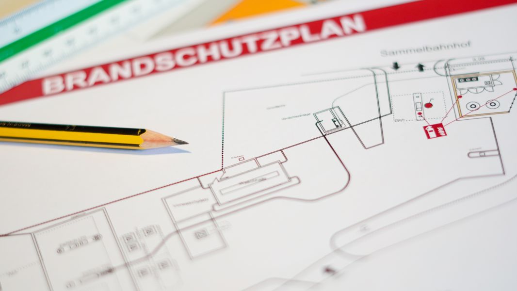 Ein gelber Bleistift liegt auf einem farbigen Brandschutzplan mit roten Linien